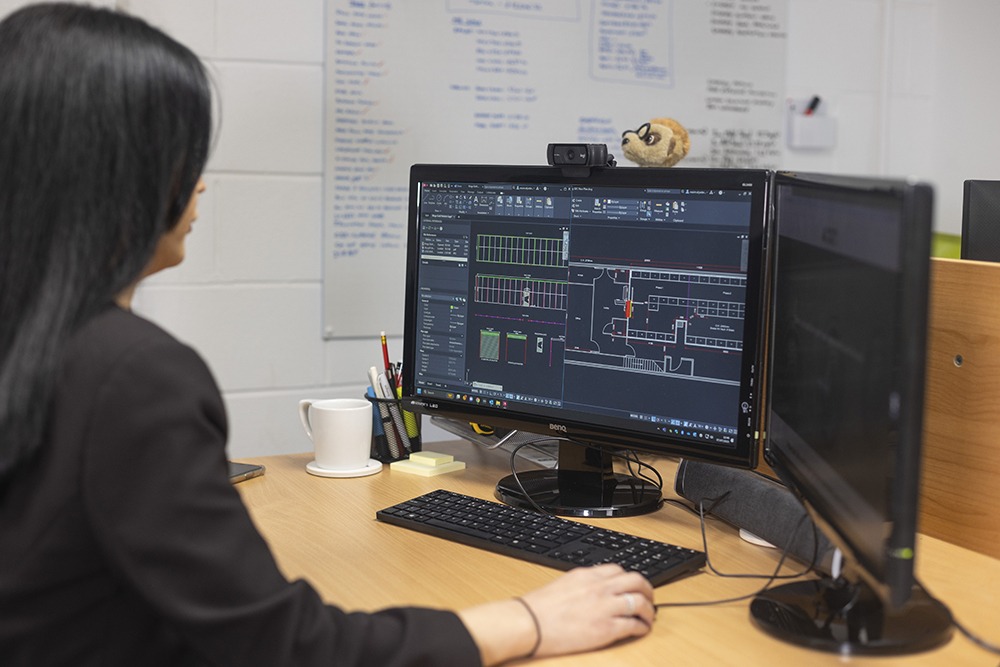 Designer working on CAD software, creating detailed plans for a panic room on a dual-monitor workstation.