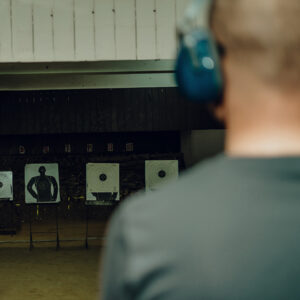A professional man wearing earmuffs and goggles is practicing shooting a 9mm pistol inside a shooting range.