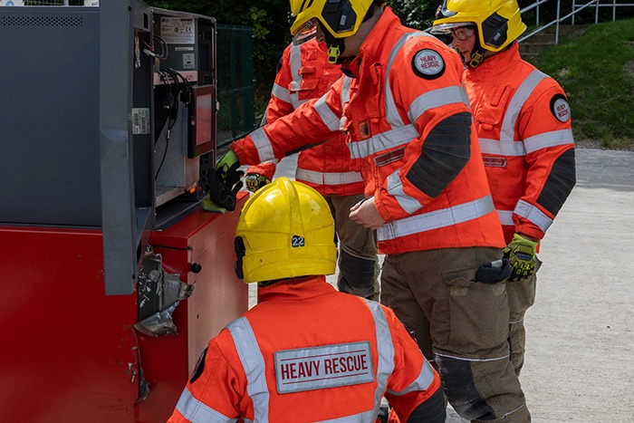 Firefighters in heavy rescue gear examine a damaged ATM during a security testing operation.