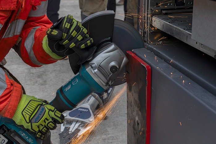Close-up of a firefighter using a power cutting tool to grind through the hinge area of an ATM unit, producing sparks.