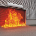 Exterior fire-rated roller shutter under intense flame conditions at an industrial facility.