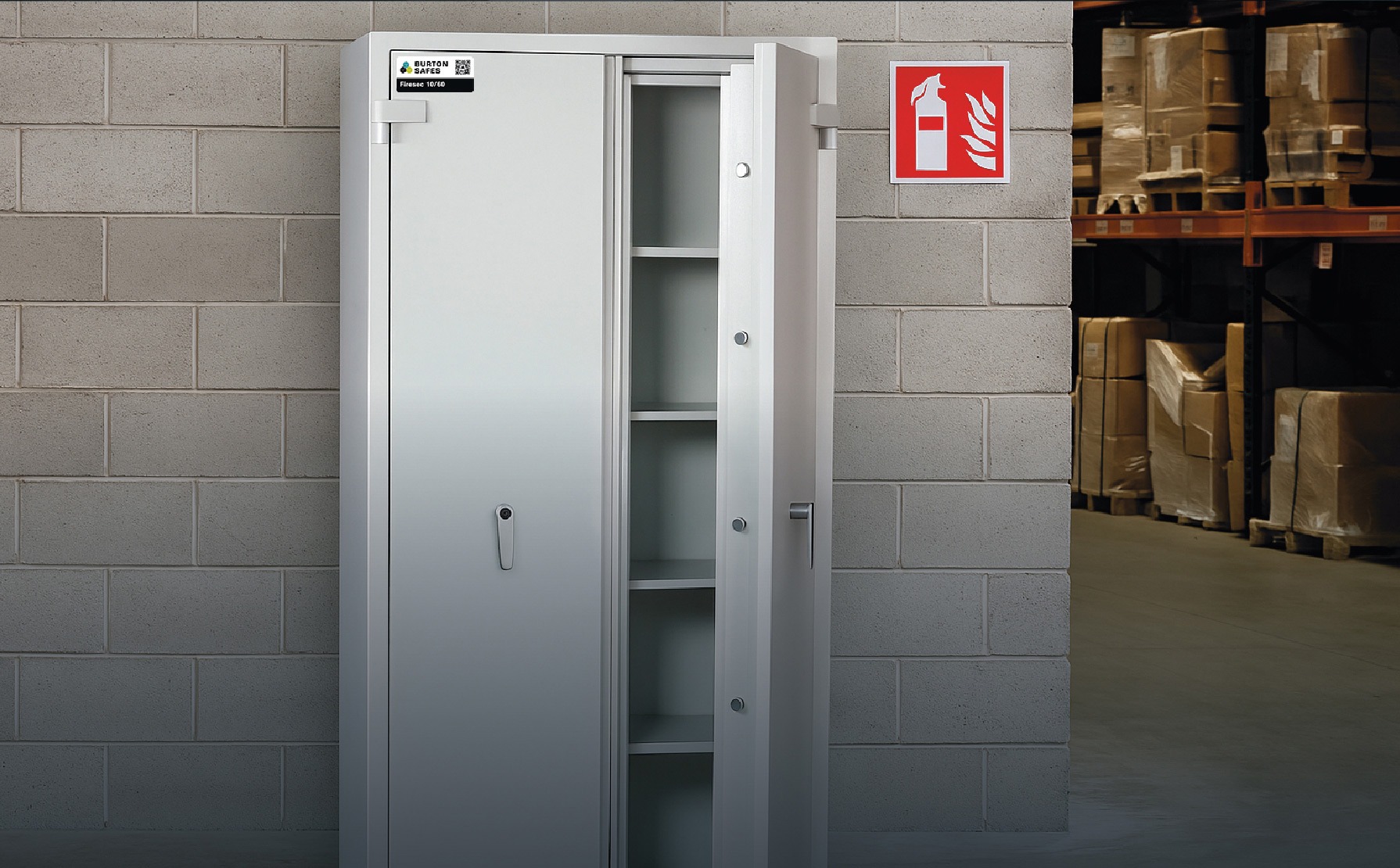 Tall fire-resistant storage safe with double doors, positioned in a warehouse beside a fire extinguisher sign.