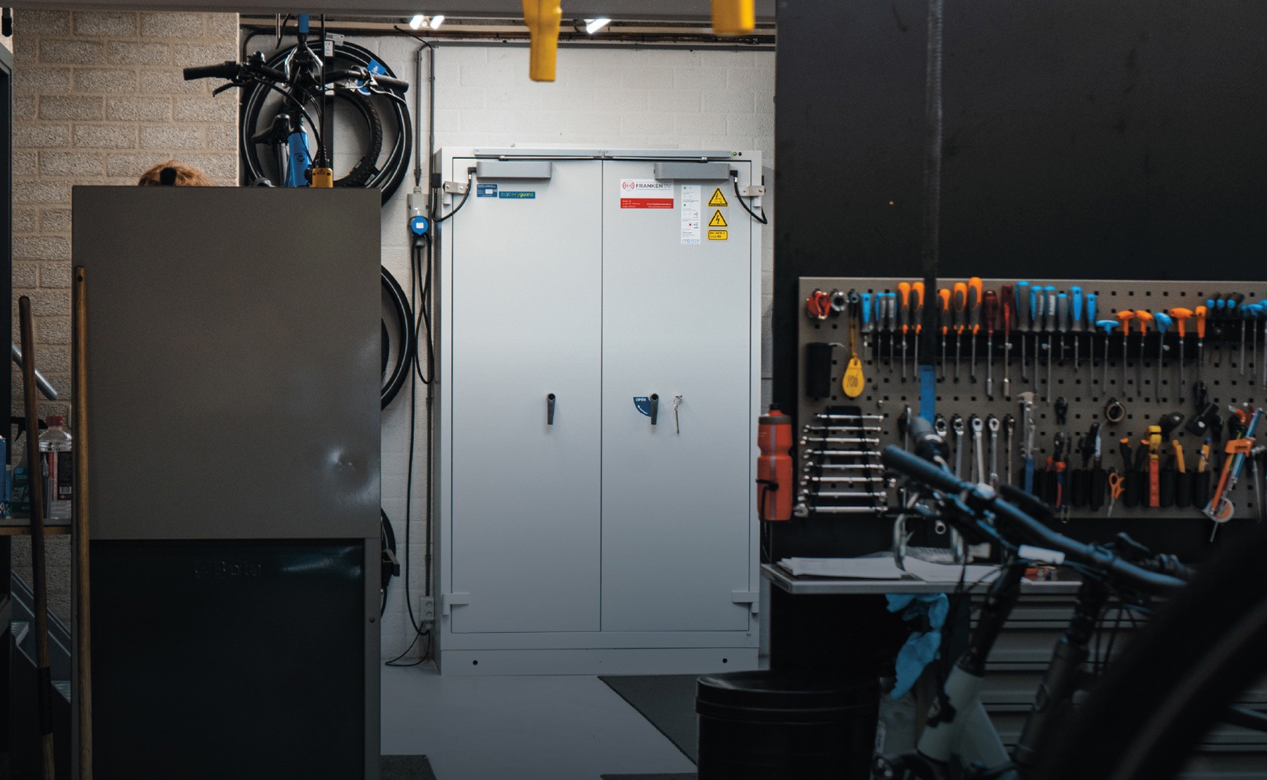 Secure lithium battery storage cabinet in a workshop, surrounded by tools and equipment.