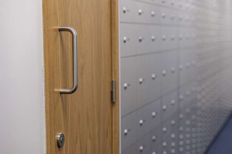 Close-up of a wooden security door with a metal handle and lock, positioned beside a secure storage wall